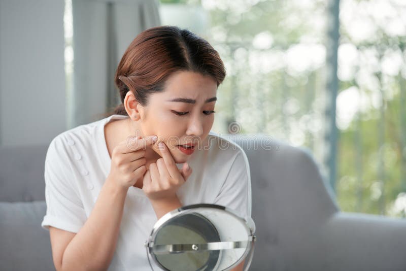 Stressed young woman examining her skin problems in a mirror