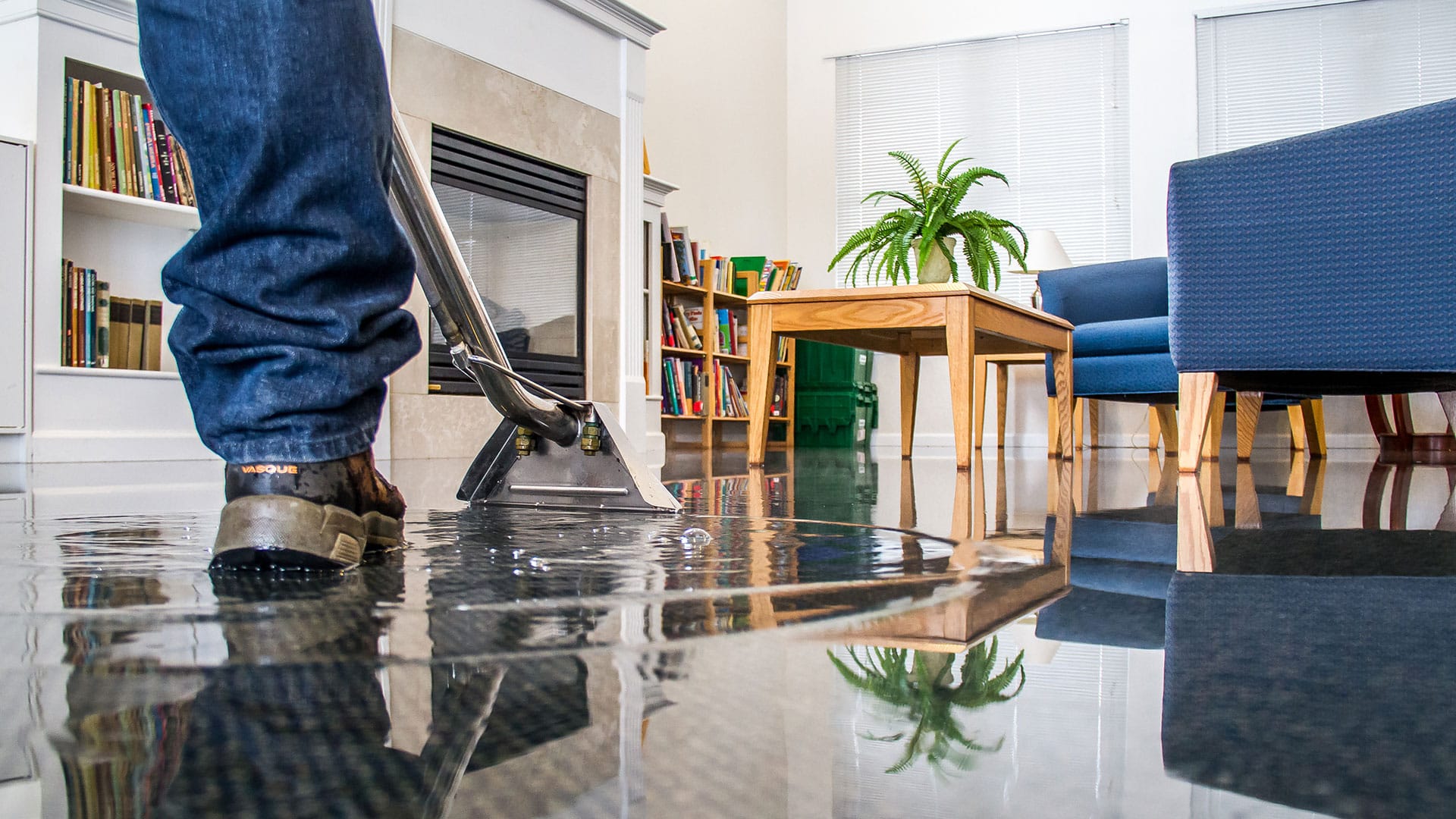 Water damage technician using a wet vacuum to extract standing water from a flooded living room floor
