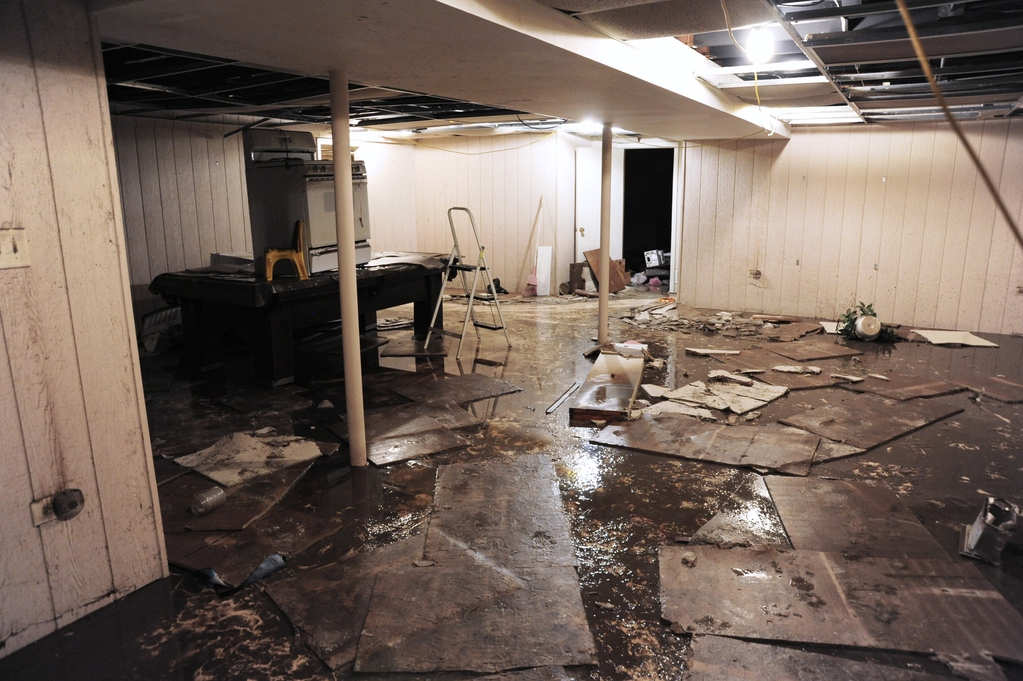 Severely flooded basement with standing water, damaged ceiling tiles, and debris requiring emergency water extraction