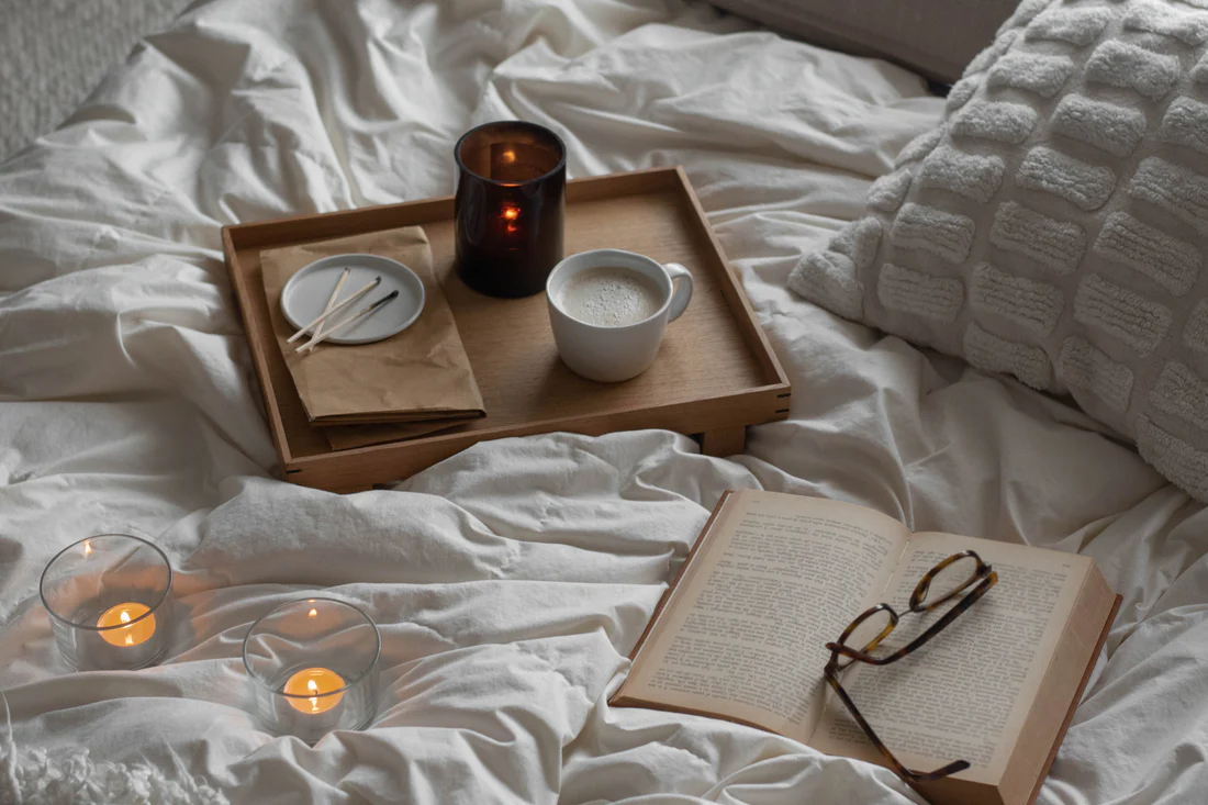 Cozy nighttime routine with candles, tea, and book on bed