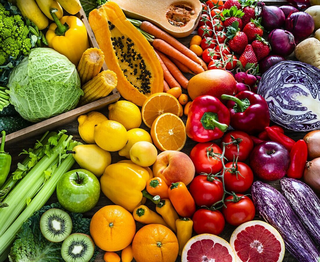 Rainbow of colorful fruits and vegetables including papaya, carrots, cabbage, peppers, tomatoes, eggplant, and berries