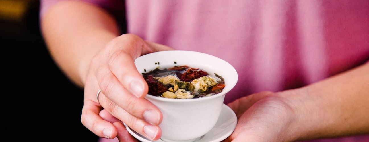 Herbal tea as a natural wellness remedy Hands holding a cup of herbal tea with dried flowers and herbs