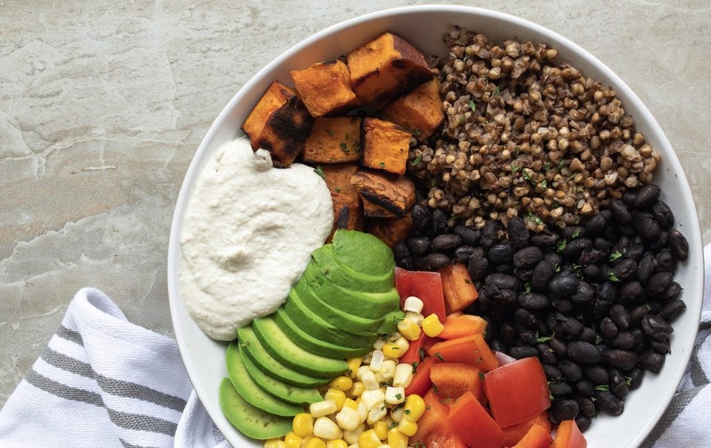 Vegan athlete power bowl with sweet potato, black beans, quinoa, avocado, and tahini dressing