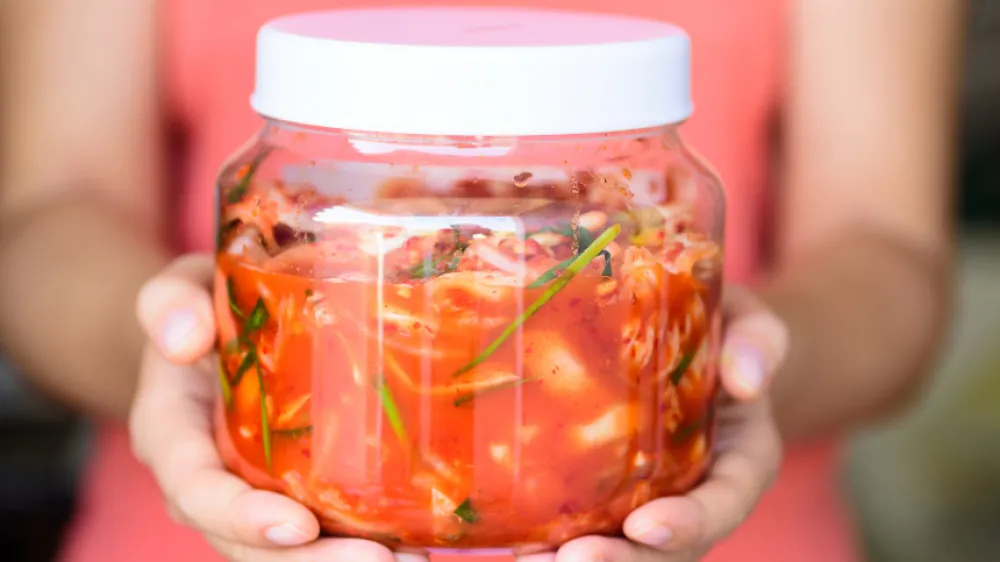 Homemade fermented kimchi in glass jar for gut health Jar of homemade kimchi being held in hands showing fermented vegetables