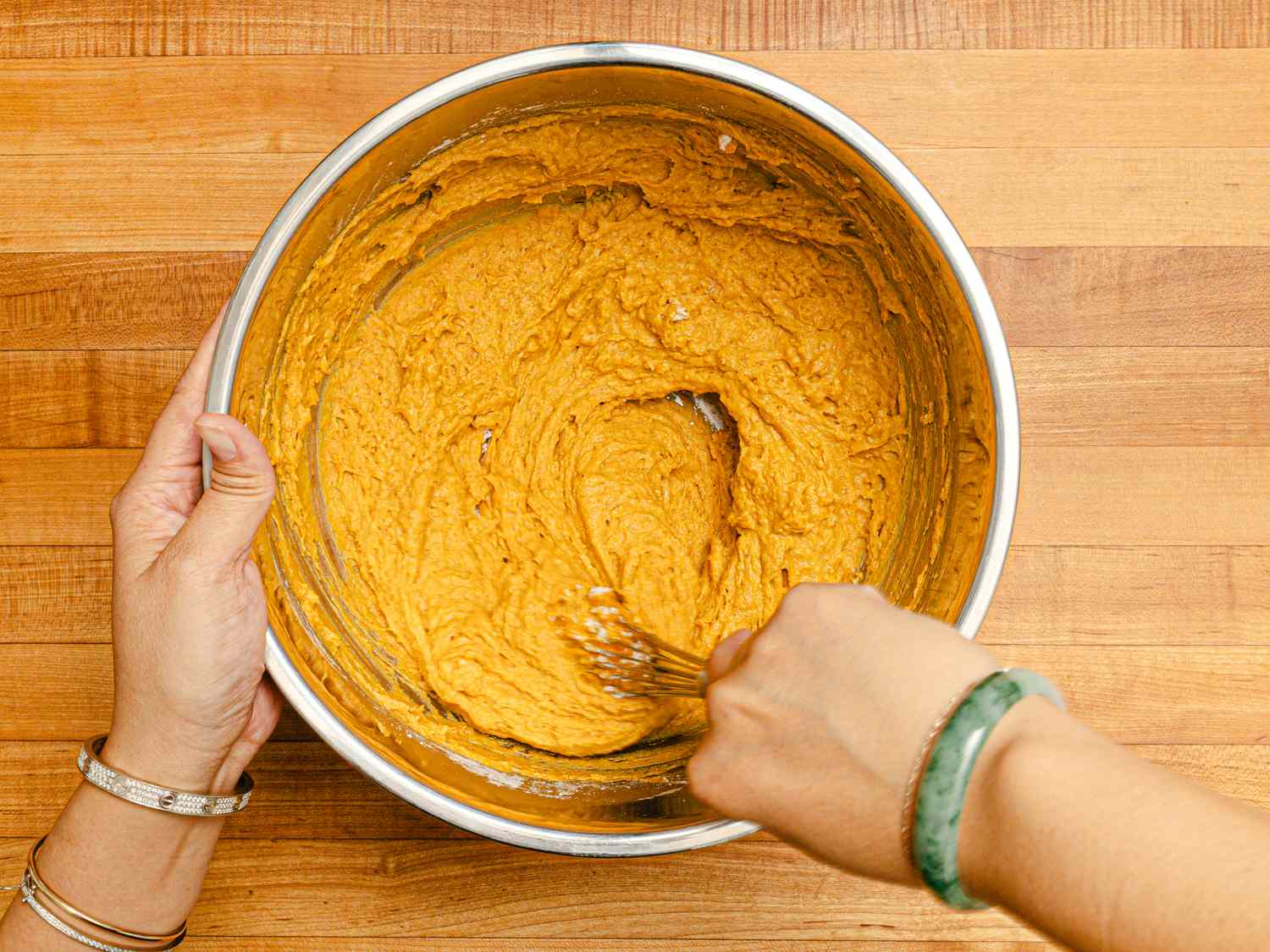 Hands mixing thick orange pumpkin paste in a large metal bowl with a spoon, showing the rehydration process