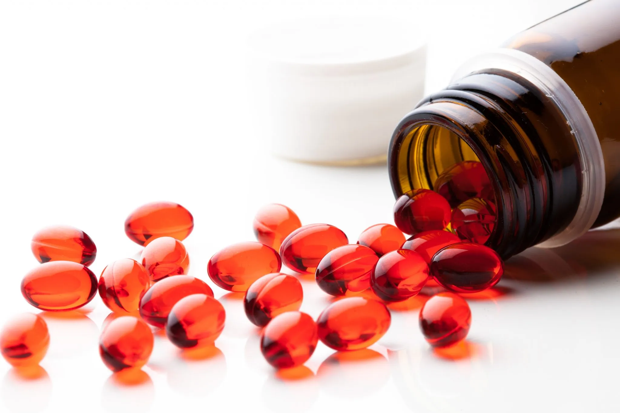 Red pharmaceutical softgel capsules spilling from amber bottle demonstrating drug delivery format