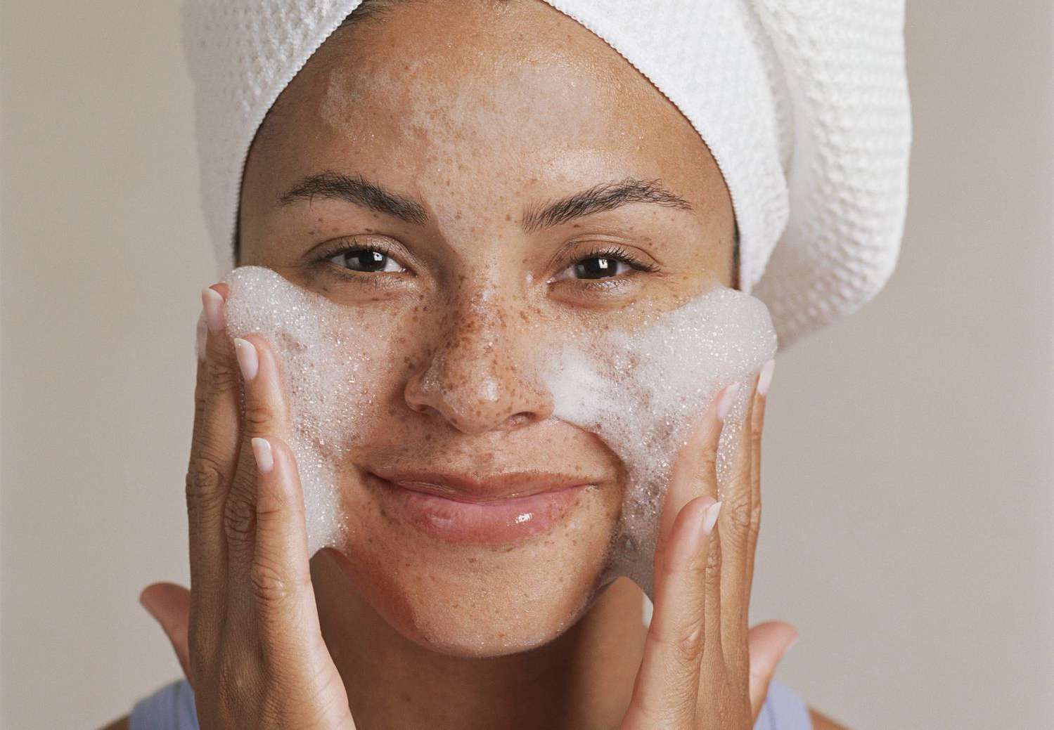 Woman gently washing face with foamy cleanser and towel wrapped hair