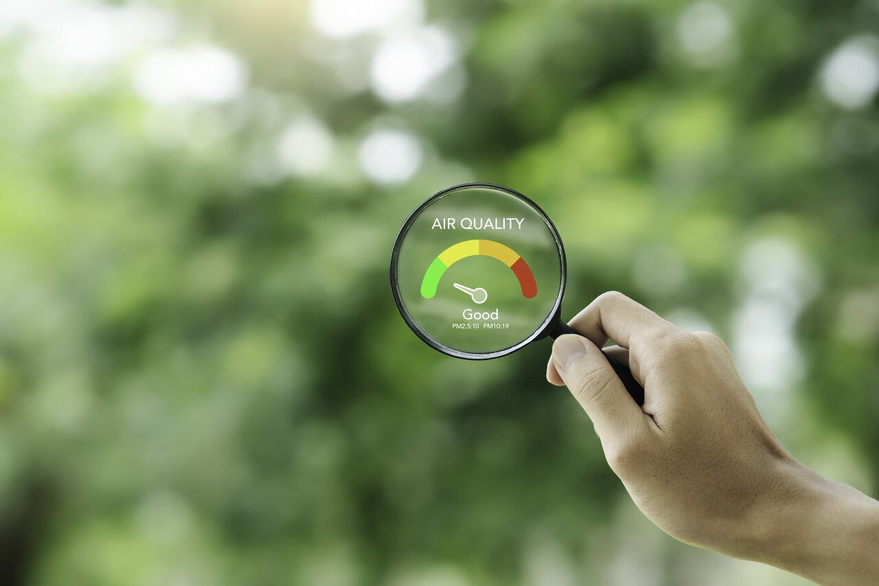 Mão segurando lupa com indicador de qualidade do ar em ambiente natural verde