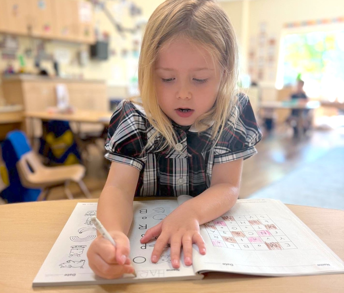 Young child practicing letter writing and early literacy skills in a classroom setting