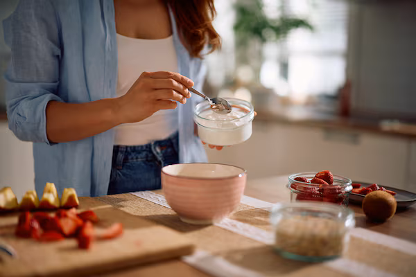 Woman preparing yogurt with fresh fruit in bright kitchen for gut health