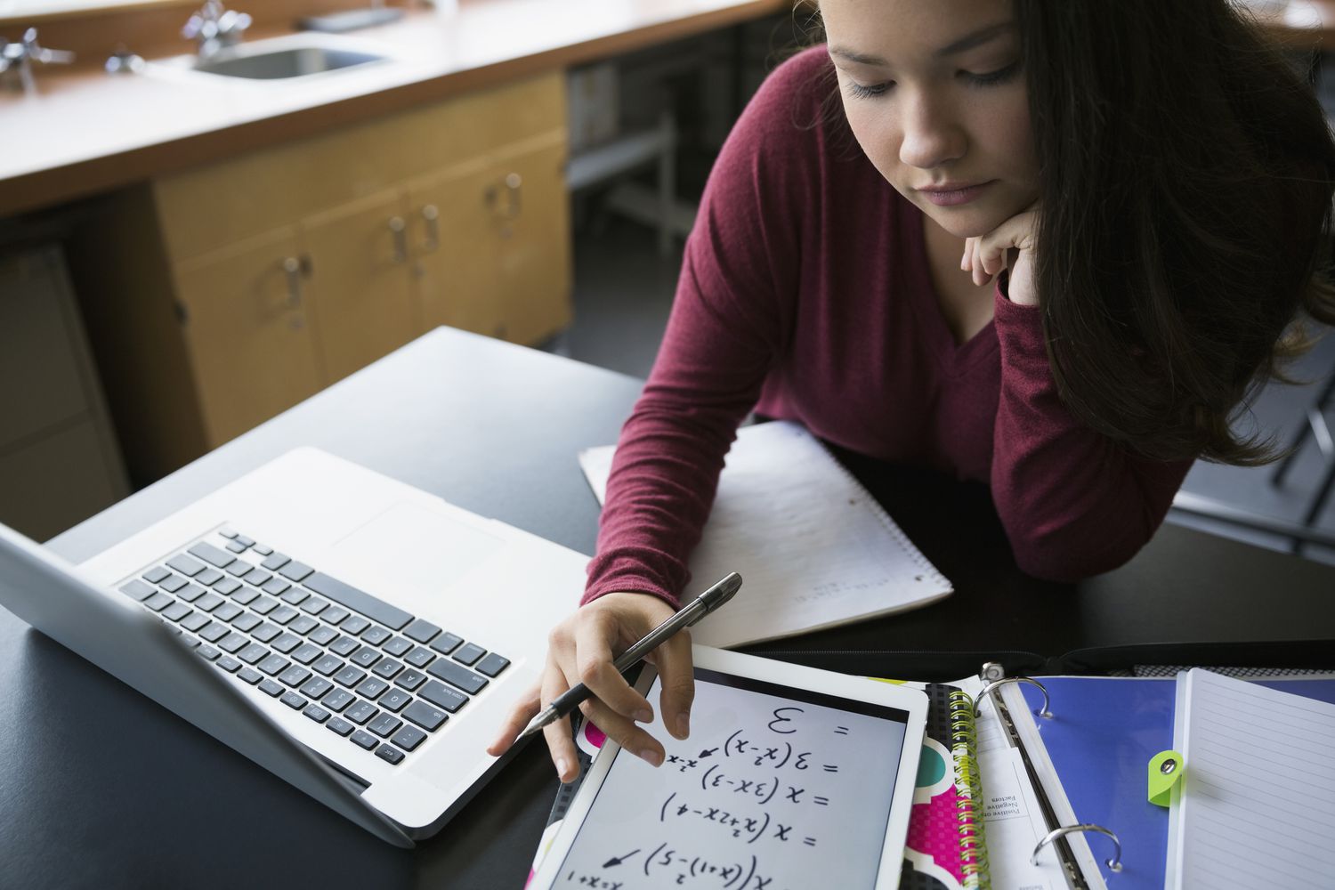 Student using tablet for online math tutoring with digital stylus and laptop