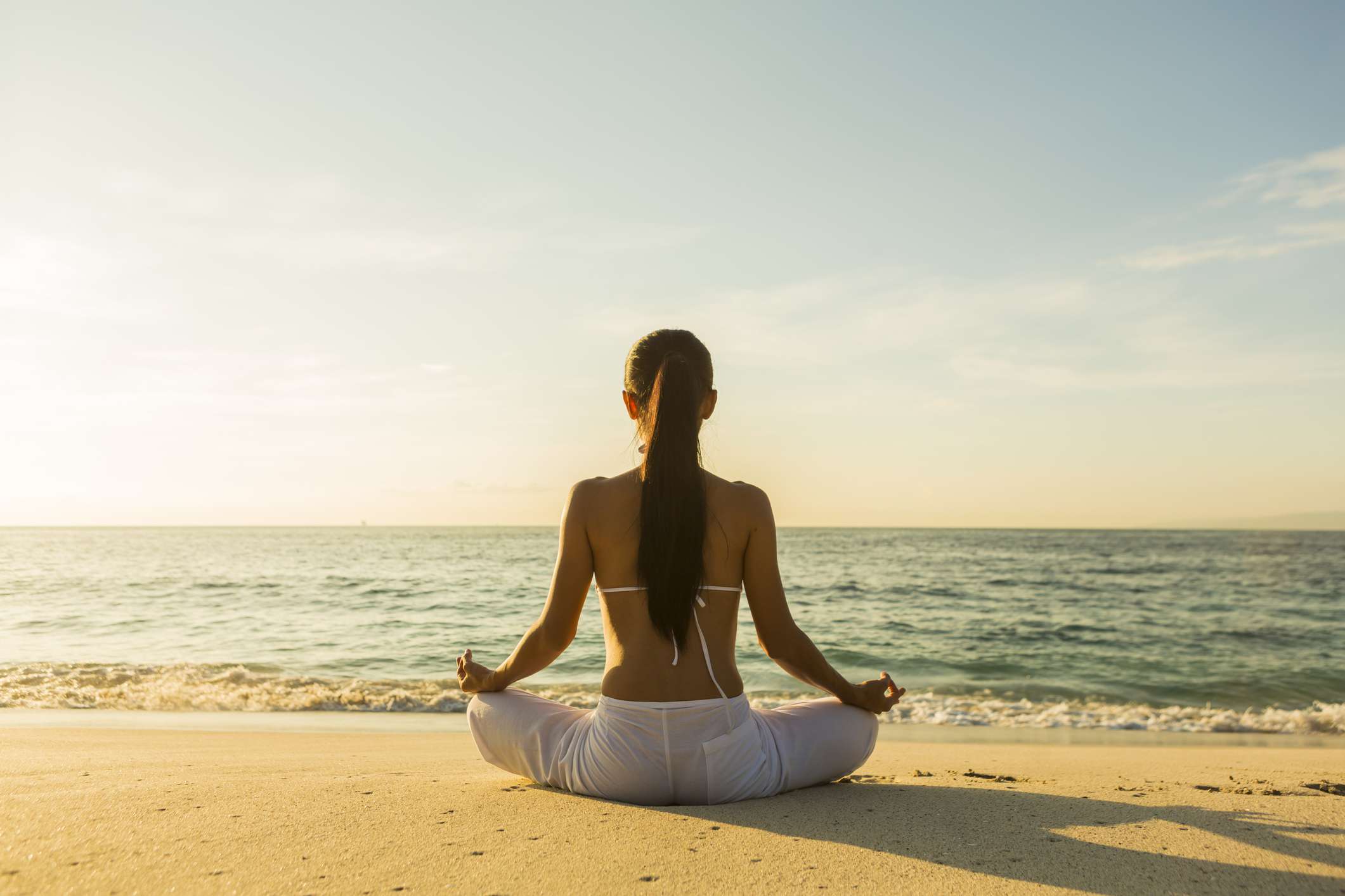 Woman practicing mindfulness meditation on beach at sunset for anxiety relief