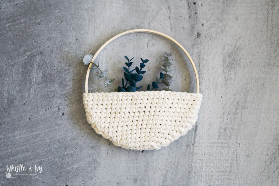 Crochet pocket planter on wooden hoop with eucalyptus stems against gray concrete wall